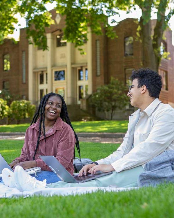 two students study on a grassy lawn